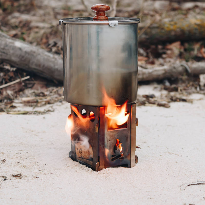 Brennender Holzkocher mit Topf beim Camping