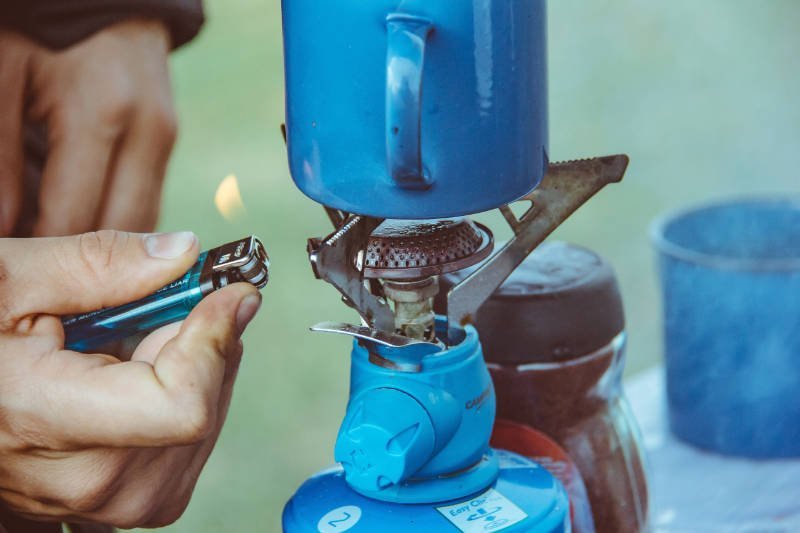 Blauer Camping Gaskocher wird von einem Mann mit einem blauen Feuerzeug angezündet