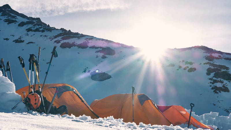 Mehrere Zelte von einem geführten Camp auf einem verschneiten Alpenberg aufgebaut.