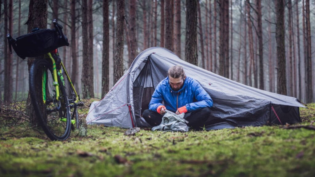 Ein Mann campt wild im Wald in Deutschland in einem ein Mann Zelt und ein Fahrrad.