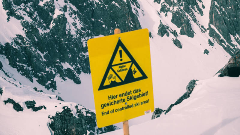 Ein gelbes Schild auf einem schneebedeckten Berg in der Alpenregion, auf dem steht: „Hier ende das gesicherte Skigebiet!“.