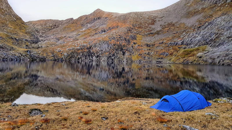 Ein blaues Zelt vor einem Bergsee: 5 Gründe, warum du das Herbstcampen lieben wirst.