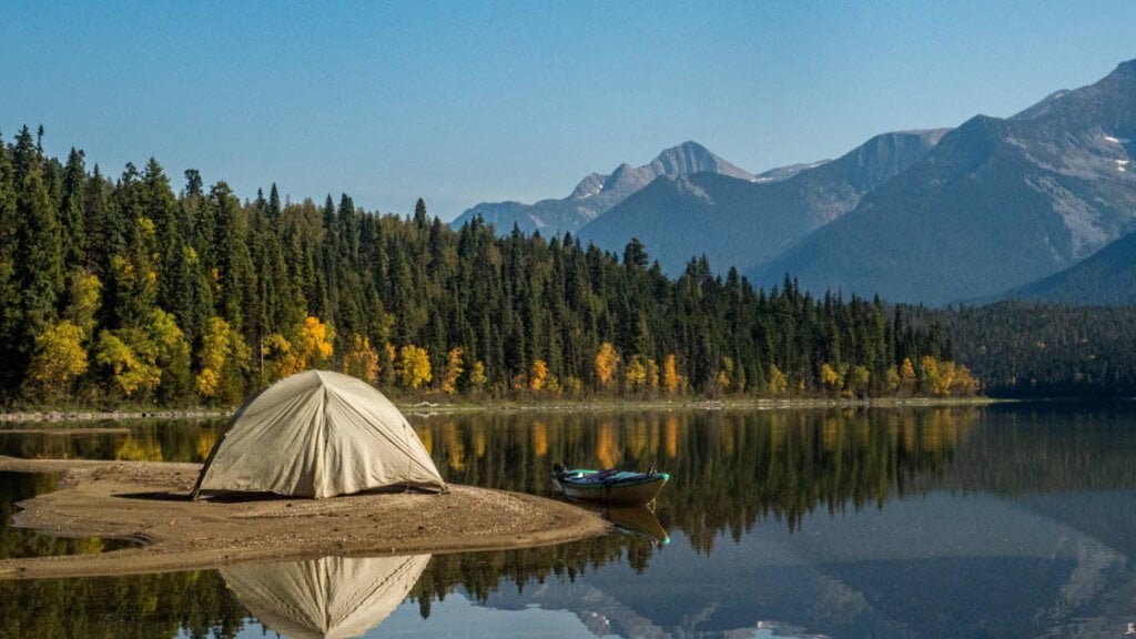 Ein Zelt steht am Ufer eines Sees mit Bergen im Hintergrund.