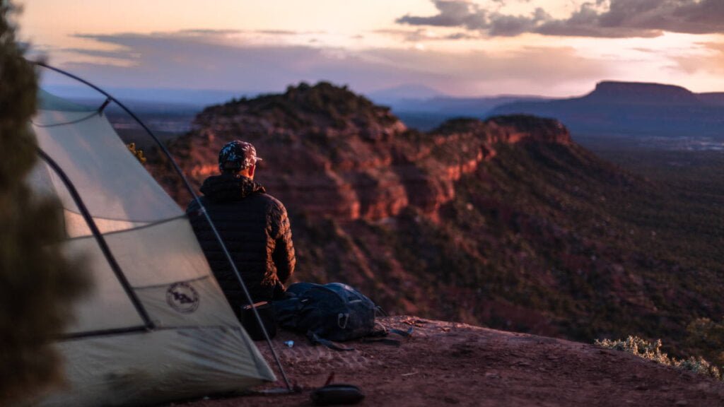 Solo-Camper genießt den Sonnenuntergang vor seinem Zelt.