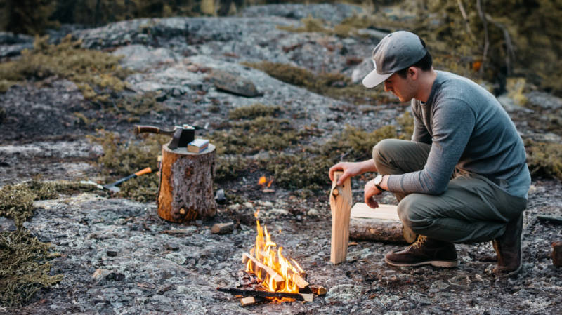 Ein Mann sitzt neben einem Lagerfeuer im Wald und fragt sich, wie heiÃŸ ein Lagerfeuer wird.