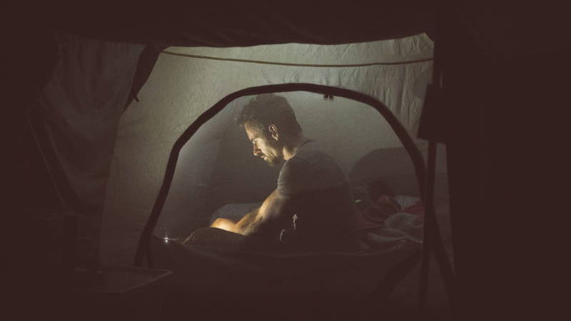 Ein Solo-Camper, der nachts in einem Zelt sitzt und ein Buch liest, um seine Angst zu überwinden.