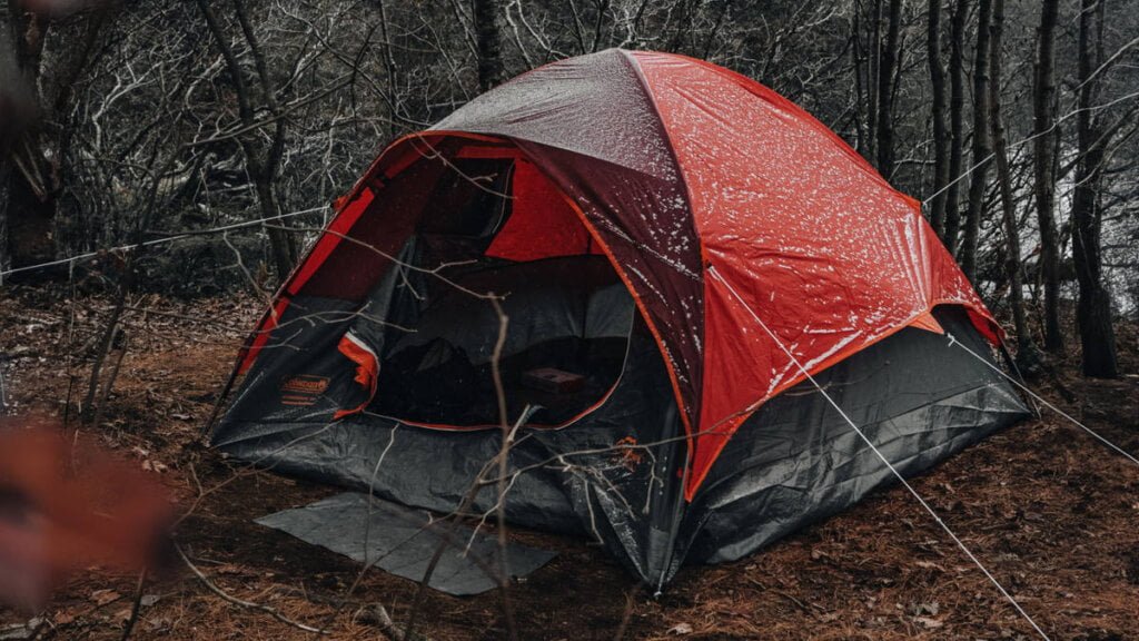 Ein rotes Zelt im Wald, befestigt mit verschiedenen Zeltheringen am Boden.