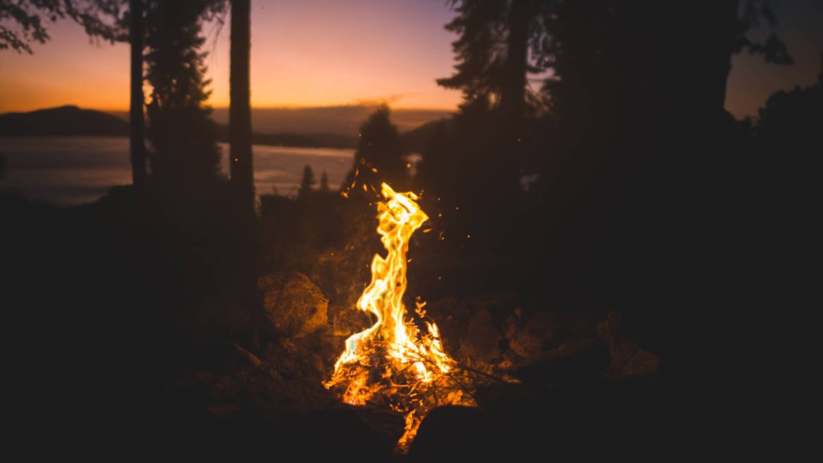 Ein feuriges Lagerfeuer, umgeben von einem ruhigen Wald und einem ruhigen See.