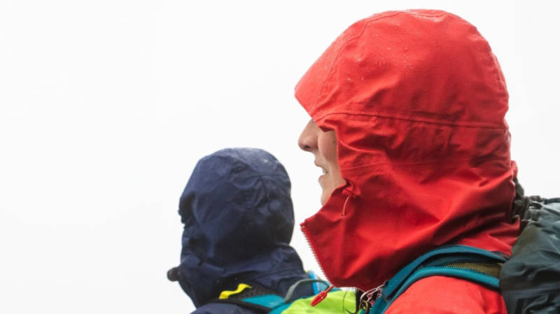 Zwei Wanderer in Regenjacken wandern an einem nebligen Tag bei Regen. Sie tragen die Kapuze ihrer Regenjacke.